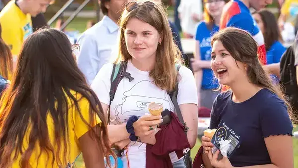 Three young women outdoors, two holding ice cream cones. One in a navy shirt laughs, while the other in white smiles.